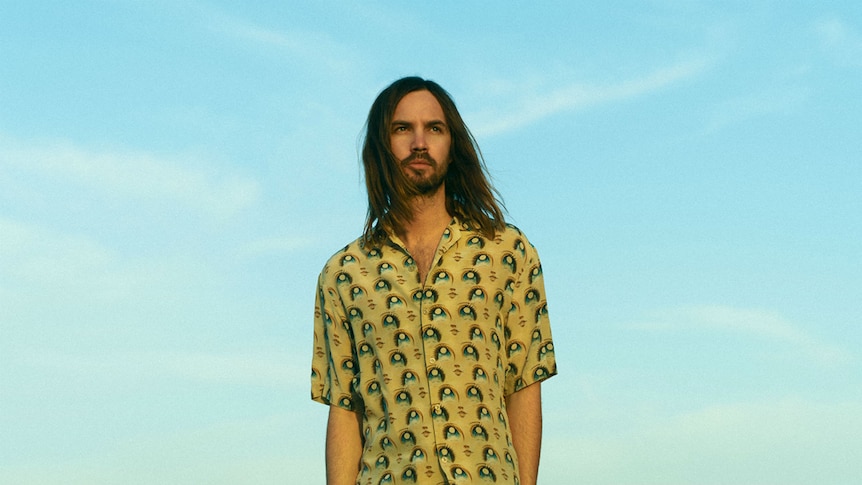 Kevin Parker of Tame Impala stands before a blue sky