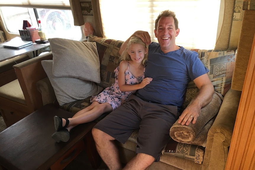 A man and a girl sit on a couch inside a mobile home