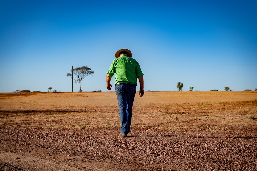 Boyd Webb walking away from camera with his head down, with flat arid land stretching into the horizon in front of him.