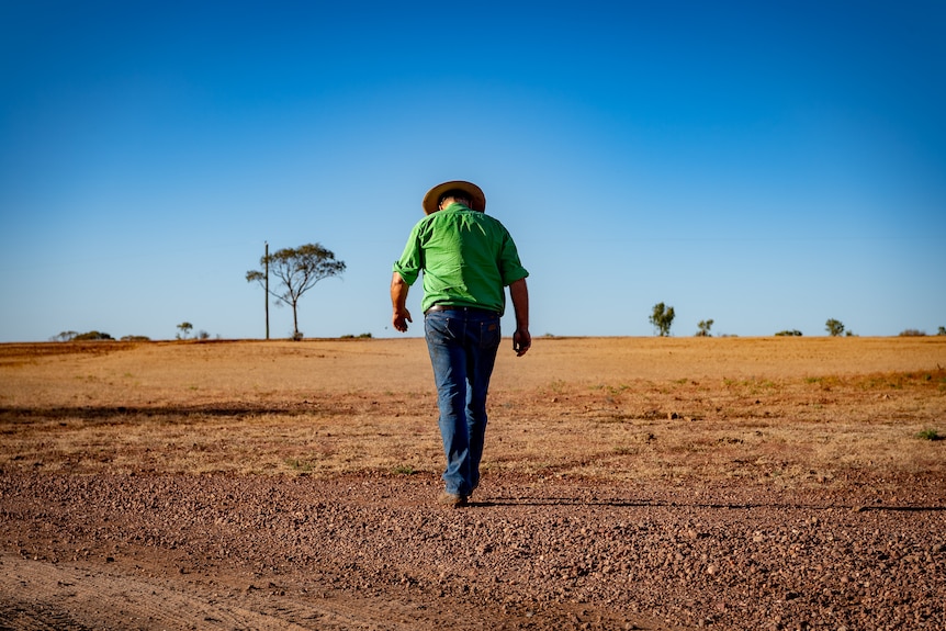 Boyd Webb walking away from camera with his head down, with flat arid land stretching into the horizon in front of him.