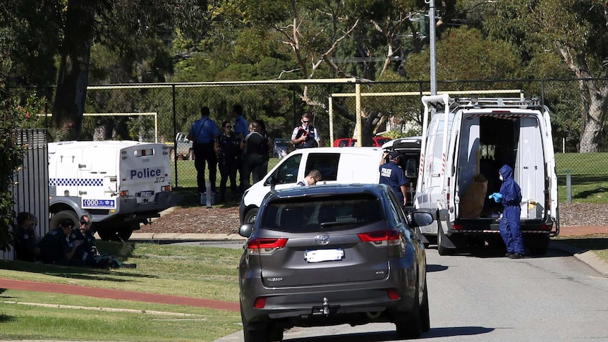 Police cars and officers on a street adjacent to a park surrounded by a cyclone wire fence.