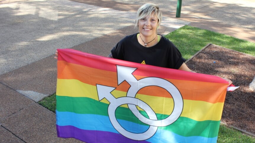 Fiona Anderson stands with a rainbow flag with equality arrows on it