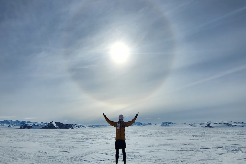 A woman standing on flat ice in Antarctica with her arms reaching towards the sun