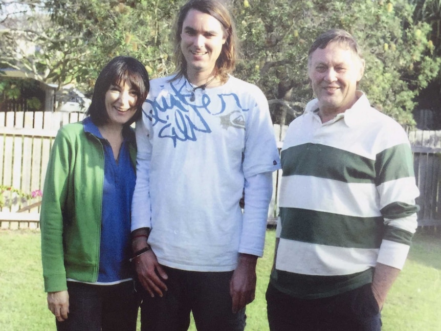 Eden Waugh stands beside his parents in a garden.