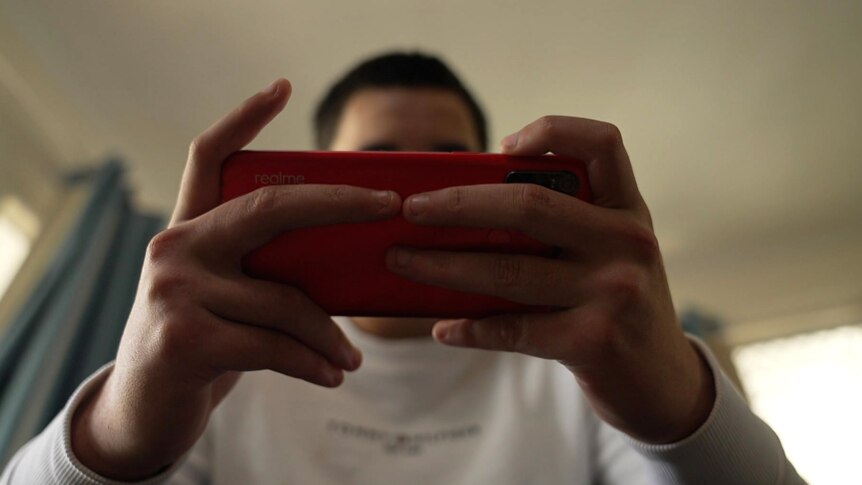 A teenager holding a mobile phone up to hide his face