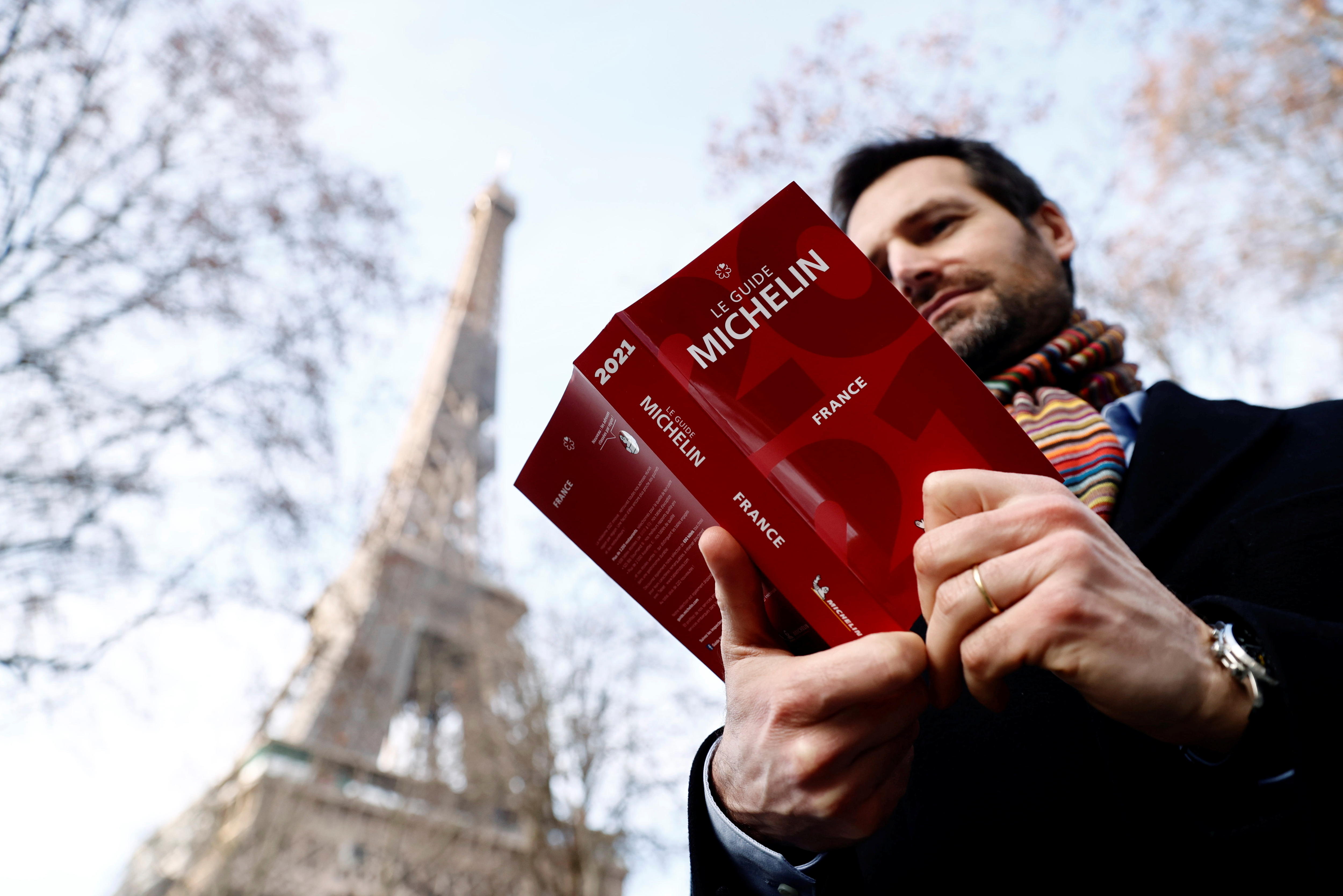 A man holding a Michelin Guide to France in front of the Eiffel Tower.