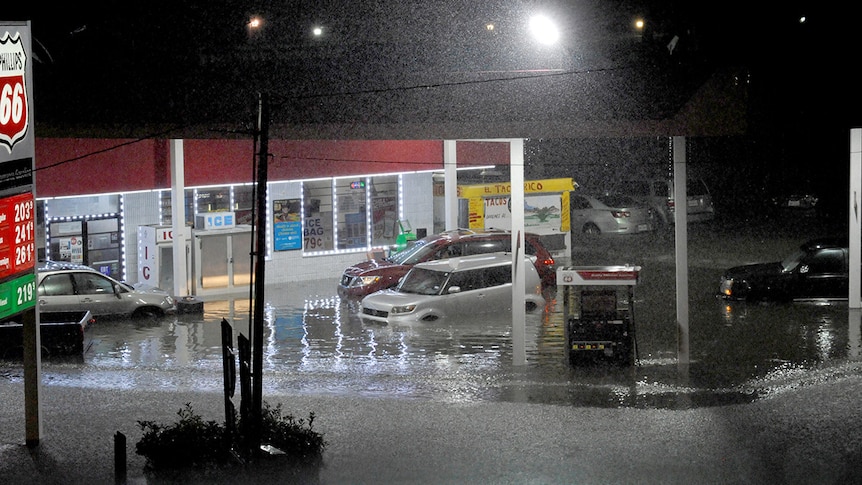 Cars sit abandoned at a flooded gas station, with water so deep it covers the rims of their tires.