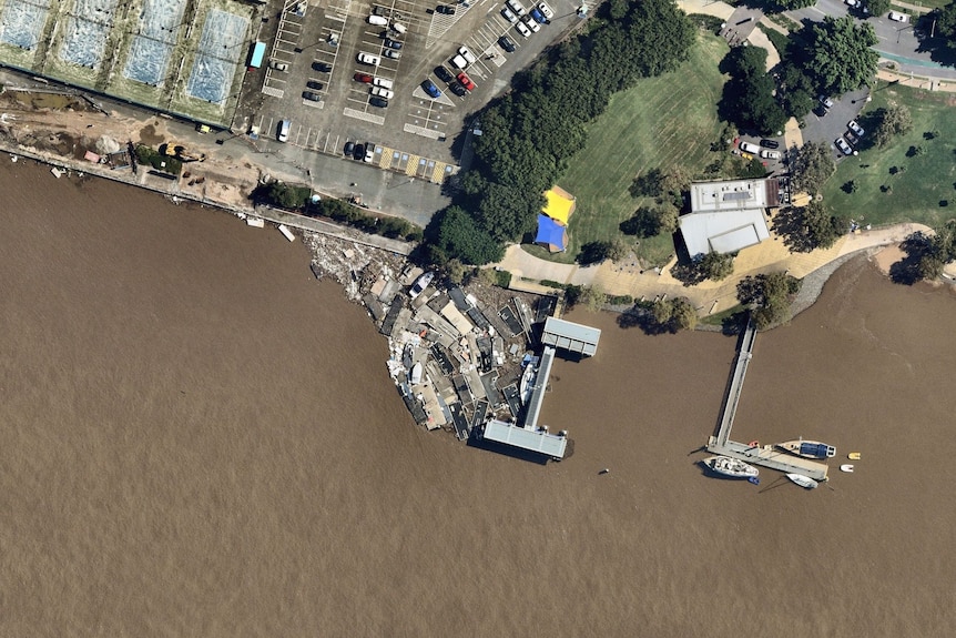 An aerial view of a flooded brown river with debris collecting at a ferry terminal.