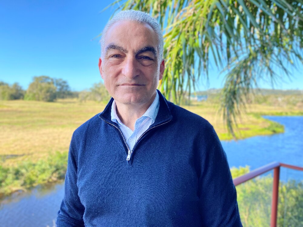 Man with gray hair looking at camera with field behind him.