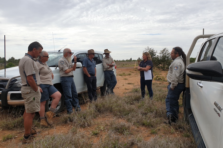 A group standing between two utes with a lady in the middle