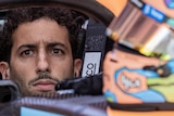 Daniel Ricciardo sits in his McLaren Formula One car with his helmet resting in front of him.
