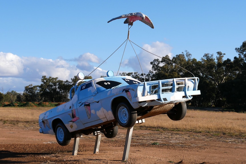 A ute painted light blue with pink and white galahs on it stands on three metal poles.