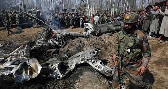 An armed soldier walks past the smoking wreckage of an aircraft as a large crown gathers around