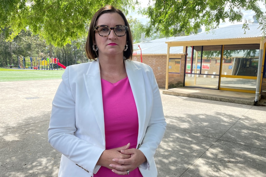 a woman wearing glasses standing outdoors at a school playground looking at the camera