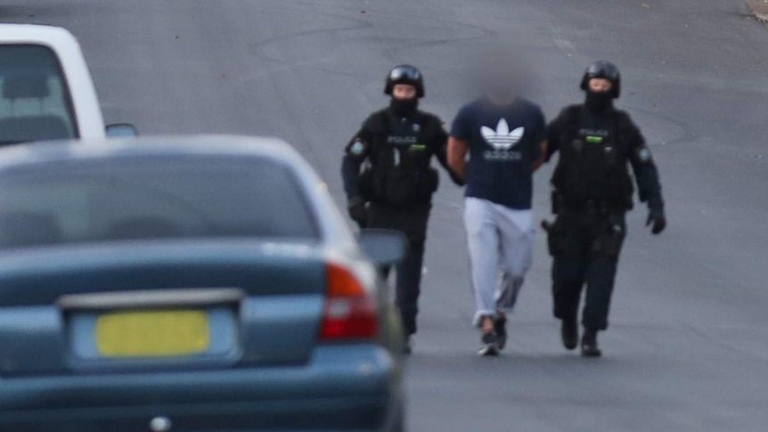 Police officers leading people away during a raid.