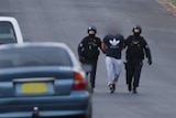 Police officers leading people away during a raid.