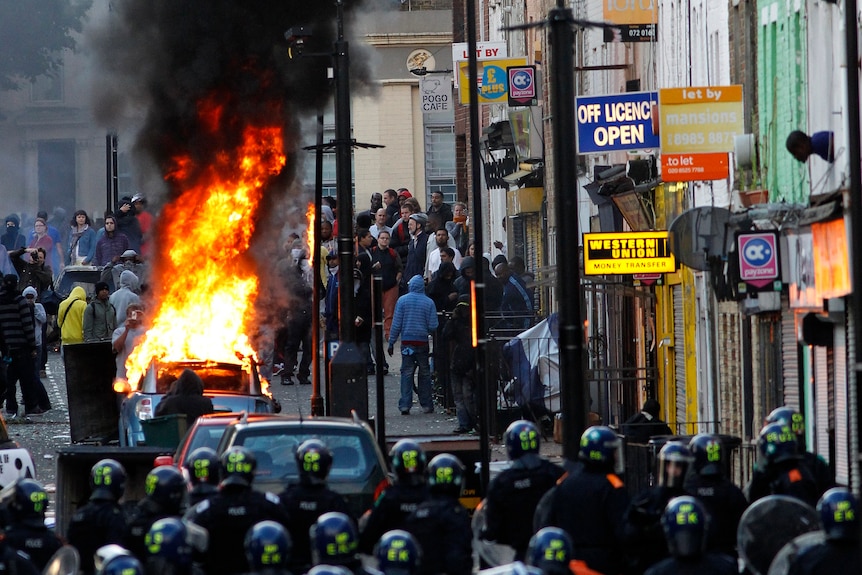 Police officers in riot gear block a road near a burning car on a street in Hackney, east London (Luke MacGregor: Reuters)