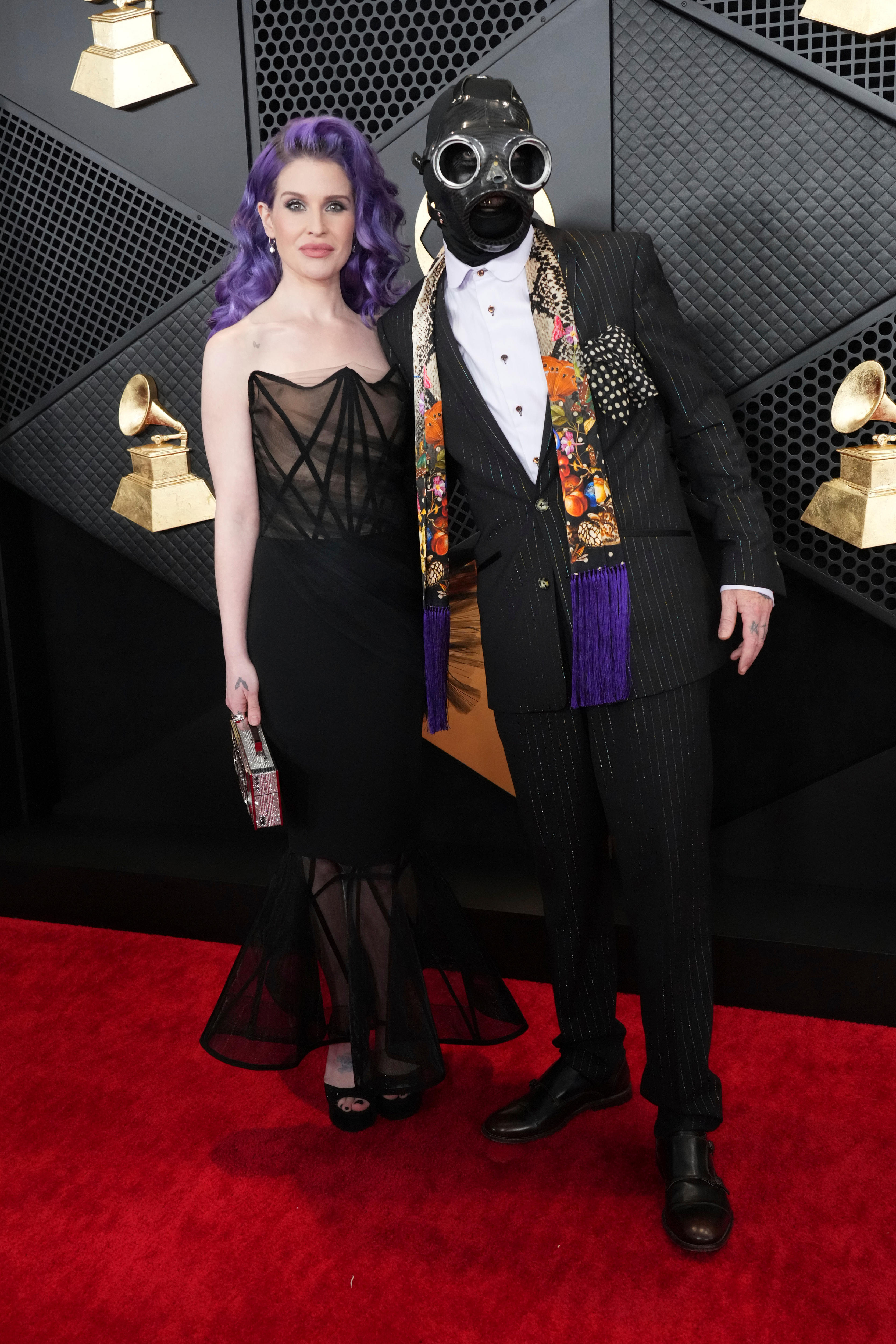 Kelly Osbourne in a strapless black dress with purple hair and Sid Wilson wearing a full-face leather mask with googles