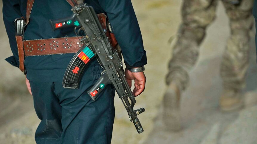 Afghan police officer walks behind a US Army soldier