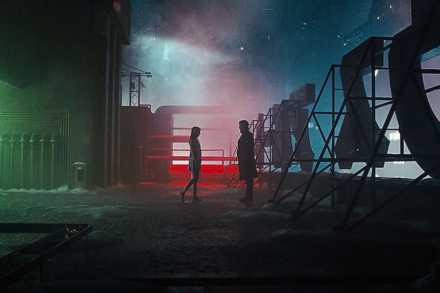 Still image from 2017 film Blade Runner on a moody and dark rooftop scene with actors Ana de Armas and Ryan Gosling.