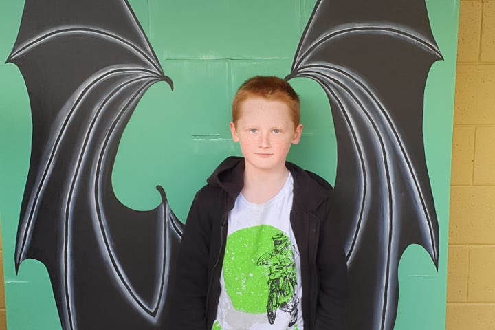 A boy stands in front of a wall with bat wings painted on it
