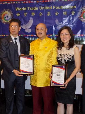 Three men in suits, two women in formal outfits, and one man wearing golden traditional Chinese shirt in front of a banner