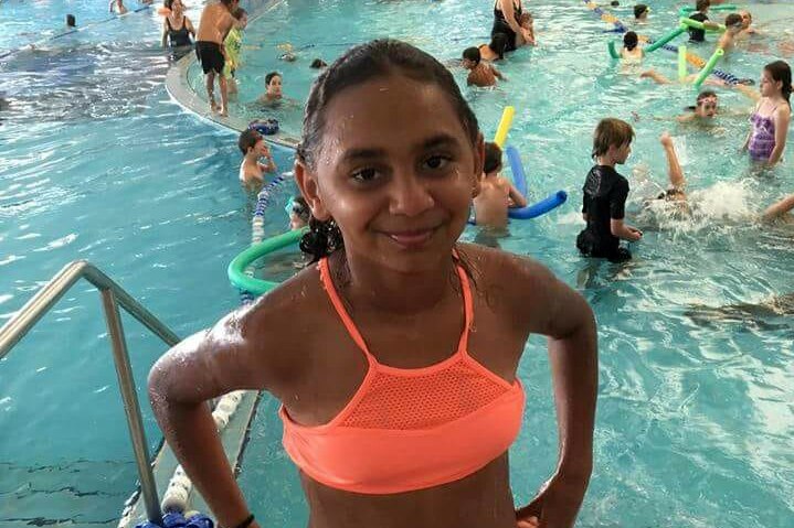 Denishar Woods in orange bathers smiling at the camera at an indoor swimming pool in Perth