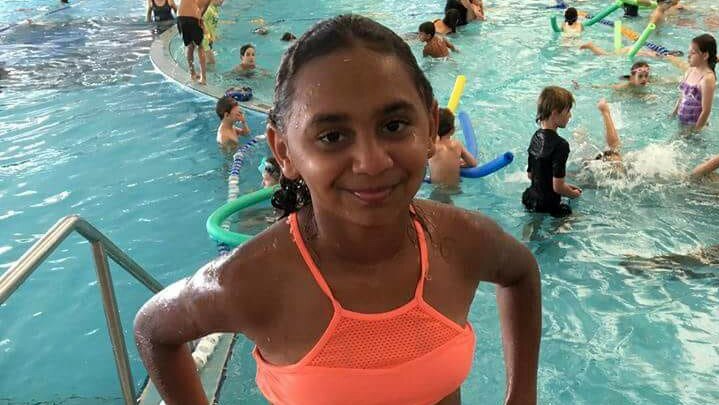 Denishar Woods in orange bathers smiling at the camera at an indoor swimming pool in Perth