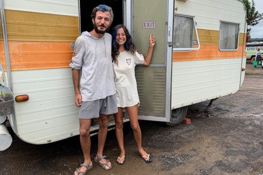 A man and woman stand in the doorway of a caravan.