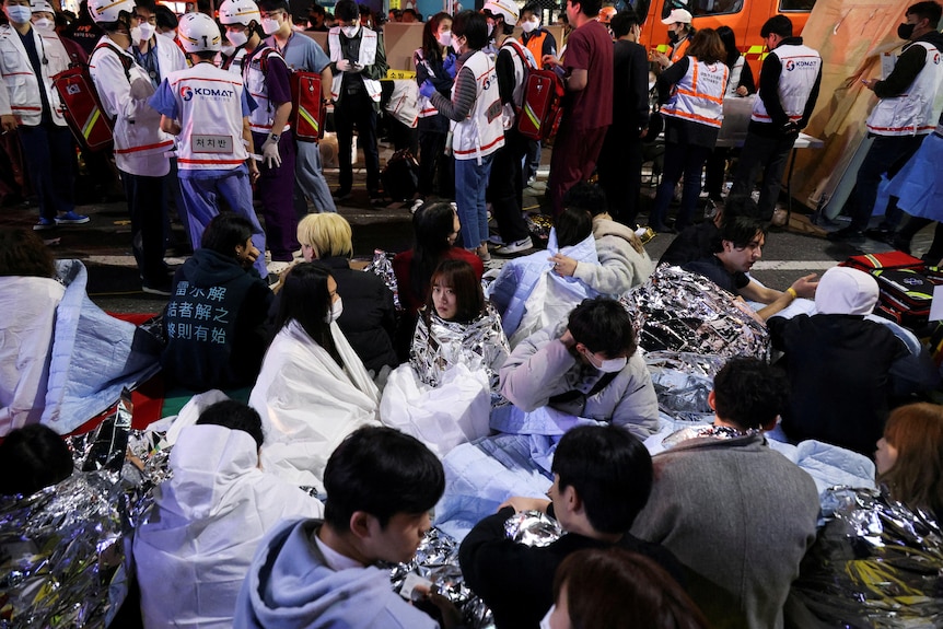 People sit on the street after being rescued at the scene of a stampede during a Halloween festival in Seoul, South Korea.