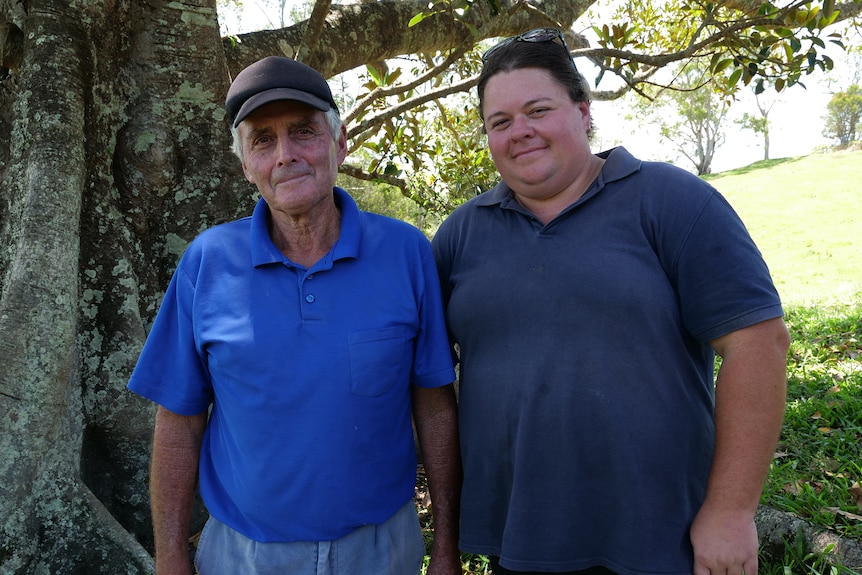 A man and woman in blue shirts stand under a fig tree.