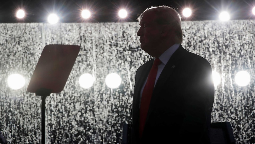 Donald Trump in silhouette standing in front of wet bullet proof glass