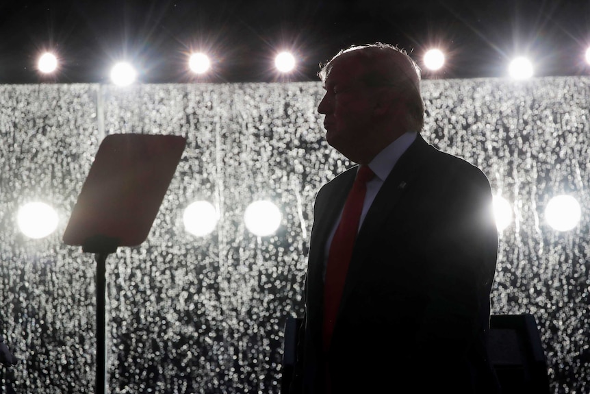 Donald Trump in silhouette standing in front of wet bullet proof glass