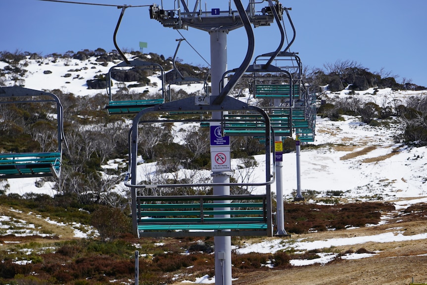 A chairlift with no one on it with patchy snow in the background.