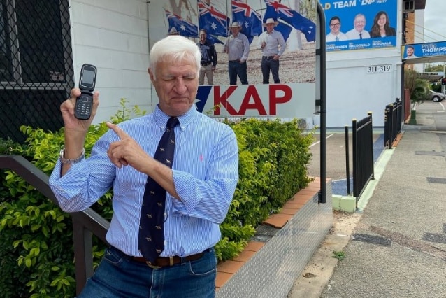 Bob Katter holding up a Nokia phone outside his office. 