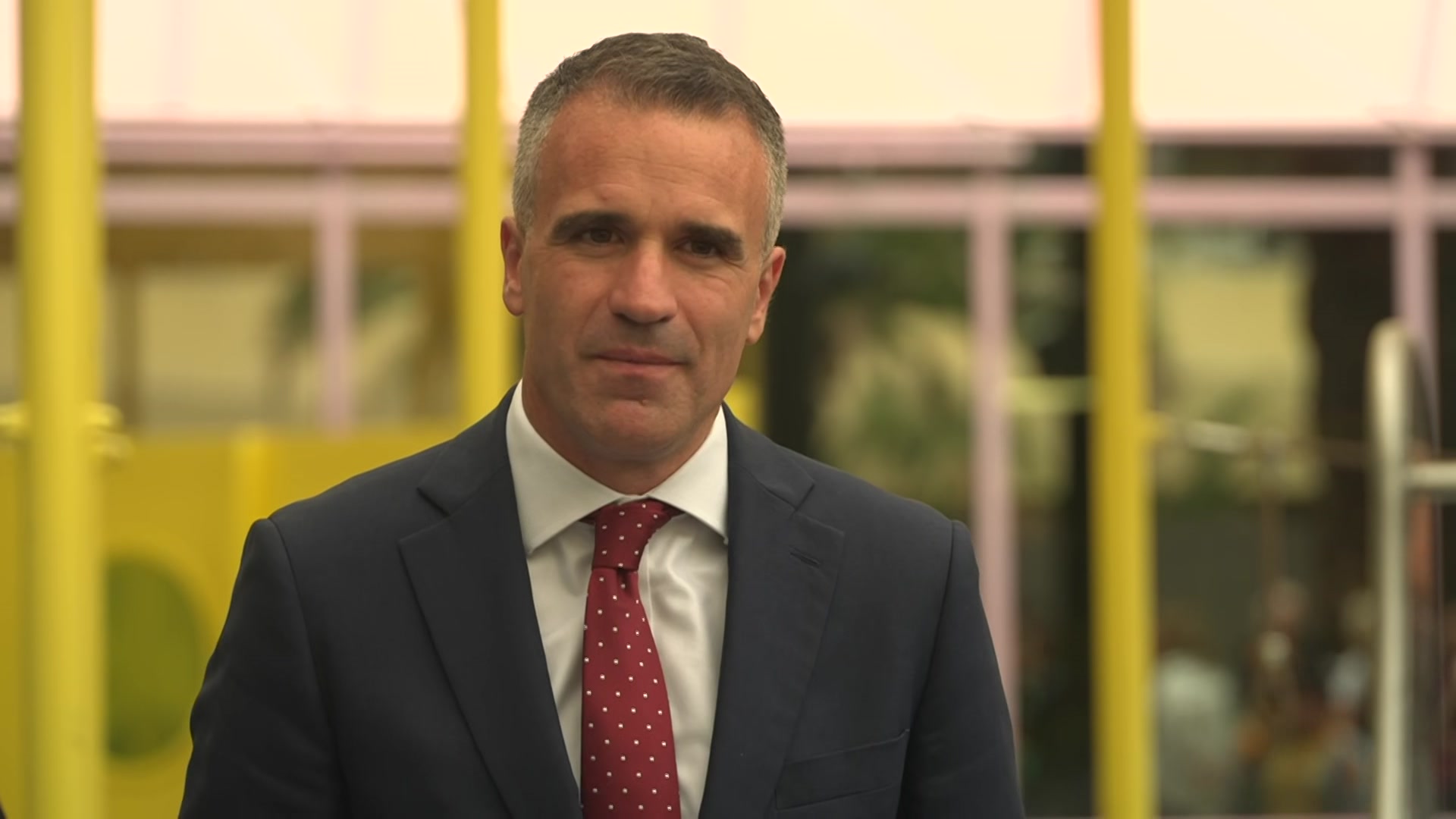 Peter Malinauskas en traje de negocios frente a las cámaras en un patio de recreo