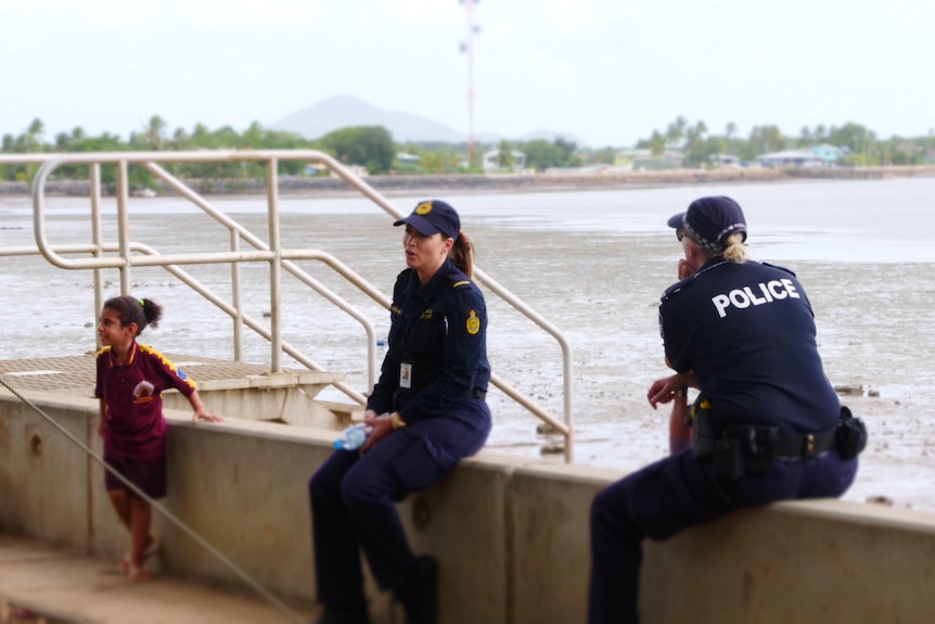 Small child stands near seated female Australian Border Force officer and female Qld Police Service officer with back to camera