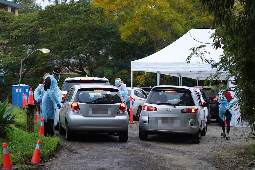 Health workers stand beside cars lined up at COVID-19 testing drive-through clinic at Toowong in Brisbane.