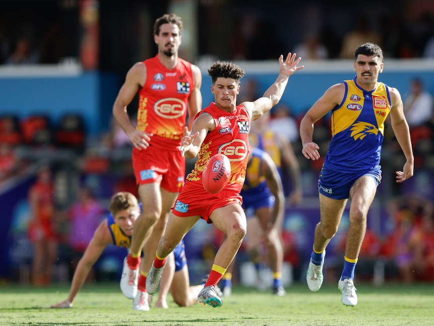 A Gold Coast player looks down as he kicks on the run for a goal against West Coast. 
