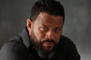 A man poses for a portrait with his arms crossed and with a serious expression.