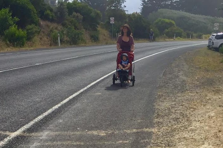 a man with a baby in a pram walking along a major road