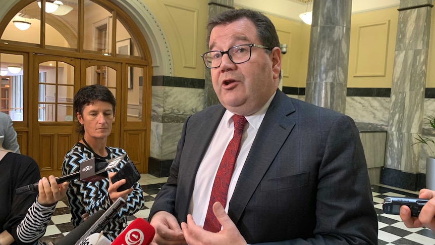 Grant Robertson, a man with a suit and glasses, speaks to reporters.