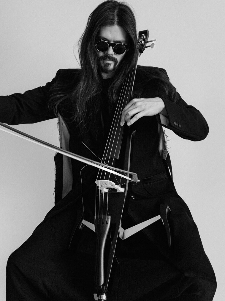 A black and white still of Benjamin Skepper looking down as he plays his electric cello.