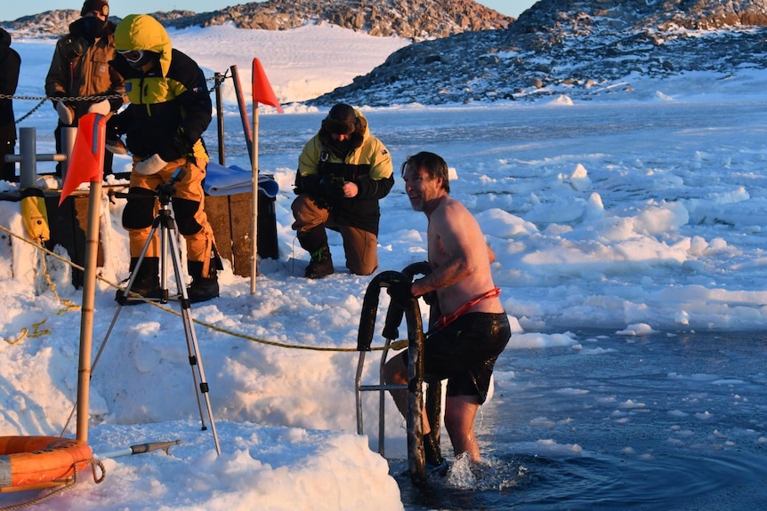 A man in black boardshorts gets up a ladder out of icy water at Antarctica 