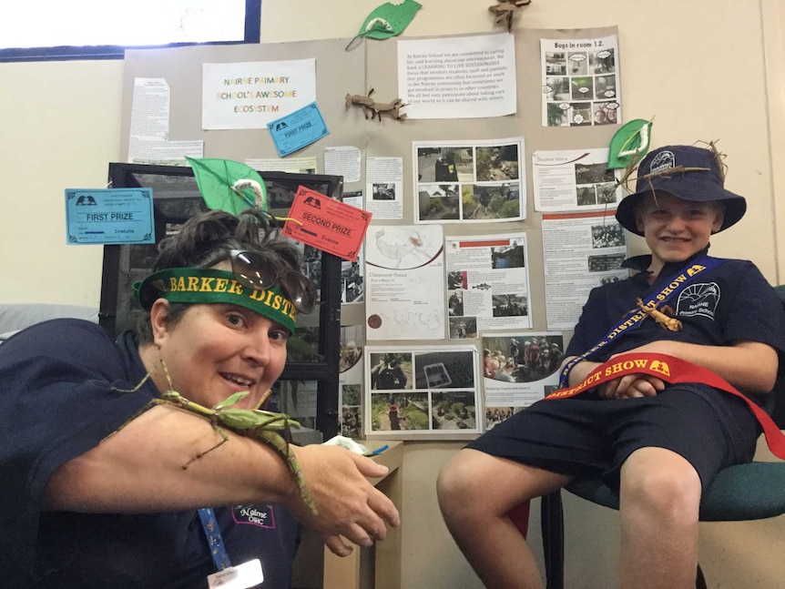 Teacher and a student show their winning ribbons beside the insect enclosures.