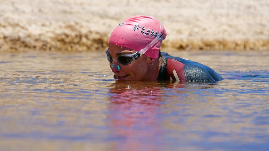 Caroline Ashby swimming in dam with swimming cap on.