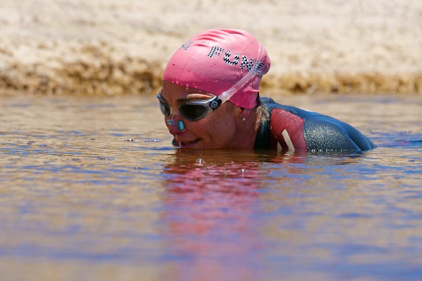 Caroline Ashby swimming in dam with swimming cap on.