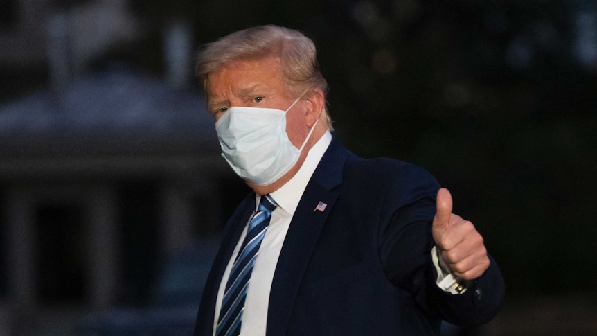 President Donald Trump gives thumbs up as he returns to the White House while wearing a mask