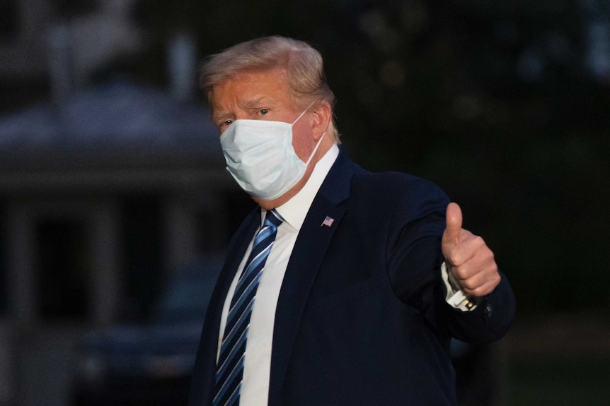 President Donald Trump gives thumbs up as he returns to the White House while wearing a mask