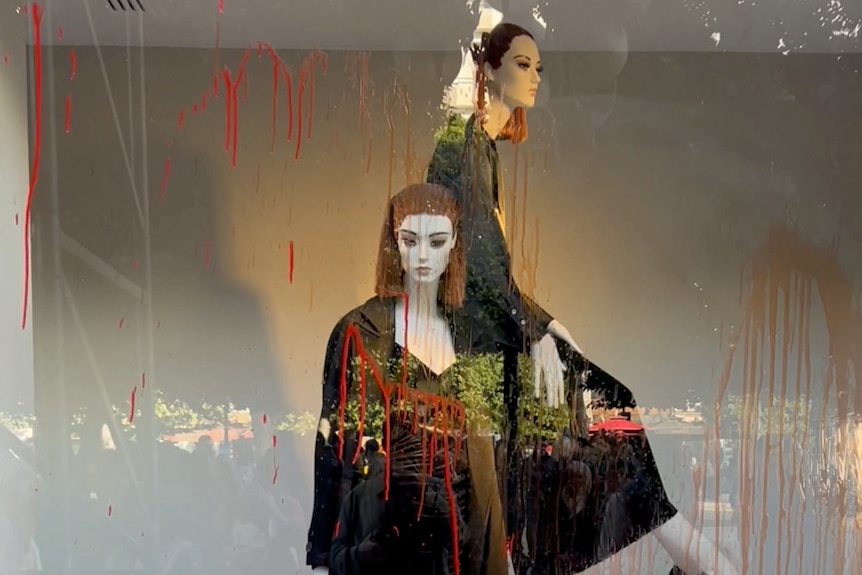 Red paint is splashed on the glass in front of two Zara mannequins. 